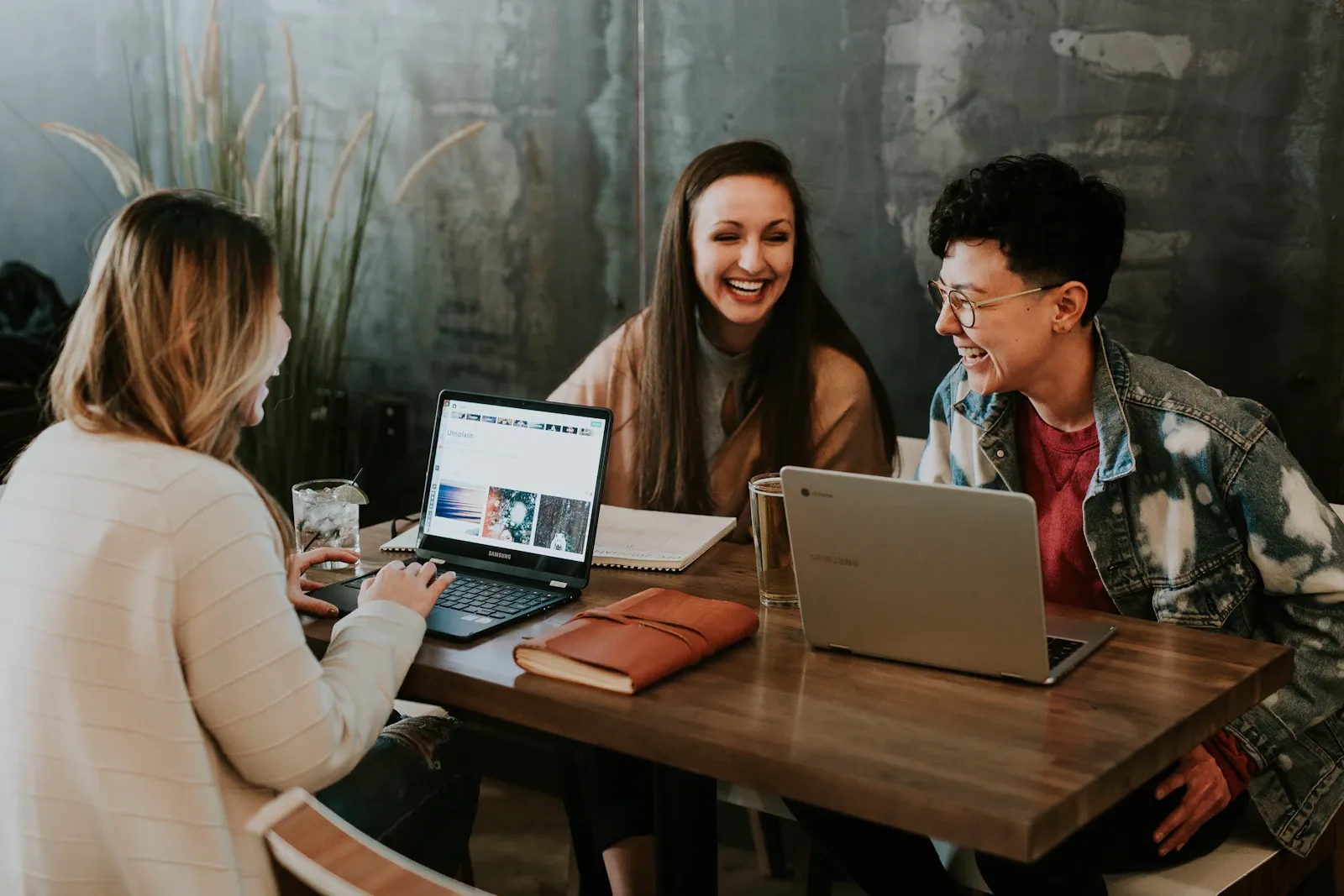 Three friends laughing together around a table with laptops